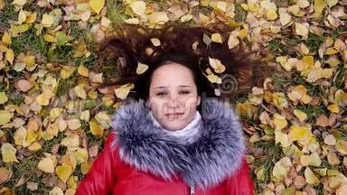 美丽幸福的年轻女子戴着耳机躺在秋叶上听音乐。 季节，科技和人